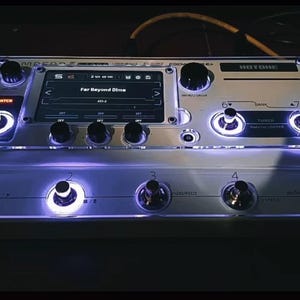 以下が含まれることがあります： 白いシルバーのマルチエフェクトペダルで、デジタルディスプレイに「Far Beyond Dime」というテキストが表示されています。ペダルには6つのノブと5つのフットスイッチがあり、周囲に白いLEDライトが点灯しています。