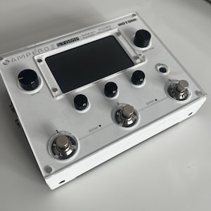 May include: White Hotone Ampero Stomp guitar effects pedal with a black and white LCD screen, two knobs, and four footswitches. The footswitches are labeled "Bank" and numbered 1 and 2. The text "HOTONE" is printed on the top right corner of the pedal.