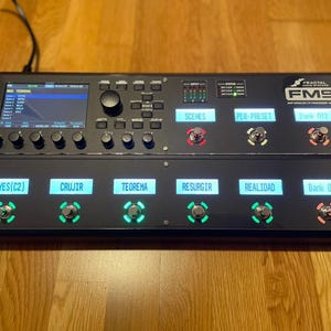 May include: A black Fractal Audio Systems FM9 multi-effects processor with a colour LCD screen, a row of knobs, and a row of footswitches. The footswitches are labelled "LEYES(C2)", "CRUJIR", "TEOREMA", "RESURGIR", "REALIDAD", and "Bank 012".