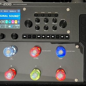 Könnte beinhalten: Ein schwarzer Valeton GP-200 Multi-Effekt-Prozessor mit einem digitalen Display, das "27-8 ORIGINAL SOUND" anzeigt. Der Prozessor verfügt über eine Reihe von Knöpfen und Reglern sowie eine Reihe von Fußschaltern mit farbigen Lichtern.