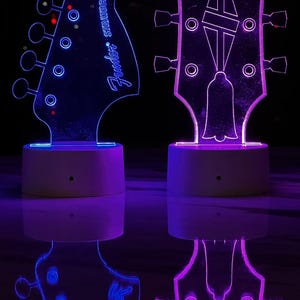 May include: Two illuminated guitar headstock night lights, one blue with "Fender Stratocaster" text and the other purple with "Gibson" text.