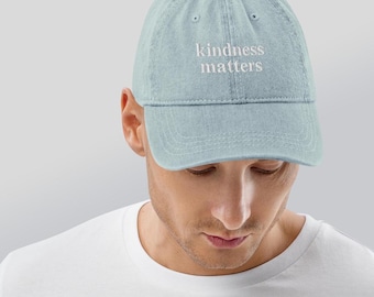May include: A light blue denim baseball cap with white embroidered text that reads "kindness matters".
