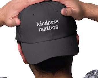 May include: A dark gray baseball cap with white embroidered text that reads "kindness matters".