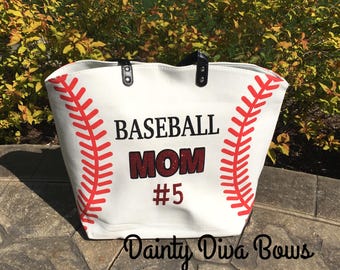 May include: White tote bag with red baseball stitching design. The bag features the words "BASEBALL MOM" with a glittery red "MOM" and the number "5". Black handles and the text "Dainty Diva Bows" are also visible.