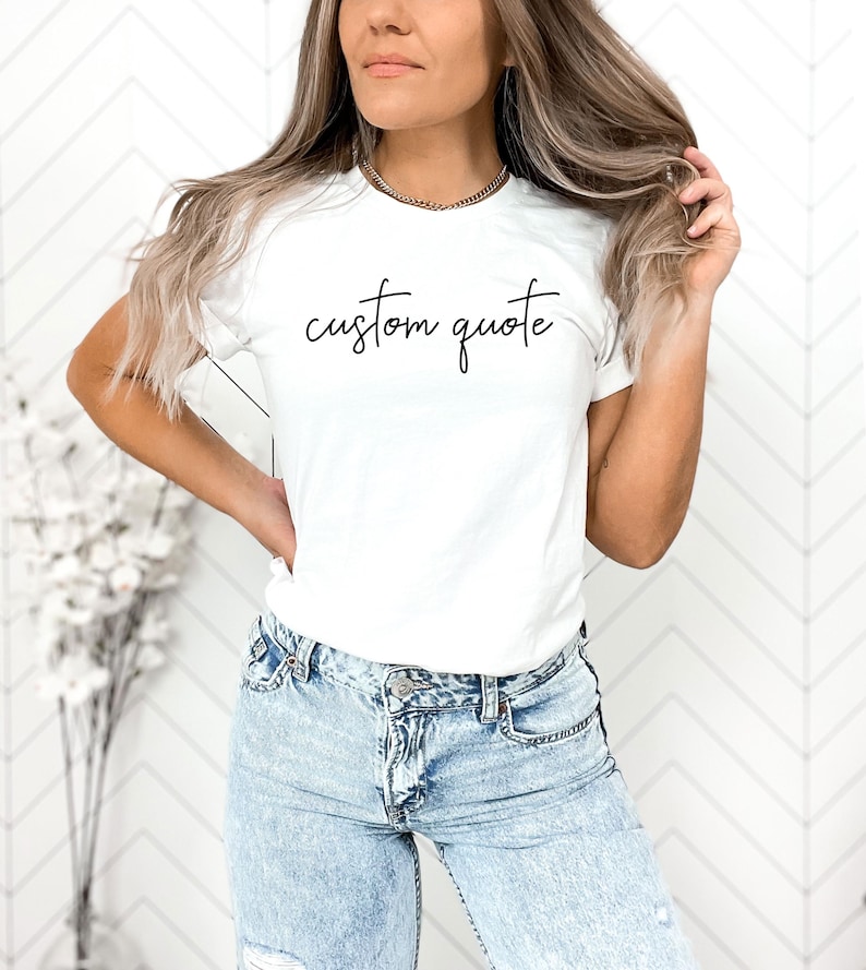 K&ouml;nnte beinhalten: Ein wei&szlig;es T-Shirt mit dem Text "custom quote" in schwarzer Kursivschrift.