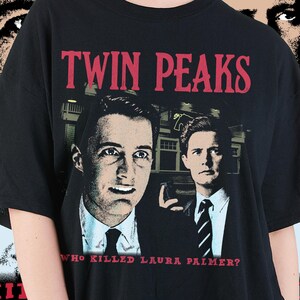 May include: Black t-shirt with a graphic print of two men from the TV show Twin Peaks. The text "Twin Peaks" is printed in red letters above the men. The text "Who Killed Laura Palmer?" is printed in red letters below the men.
