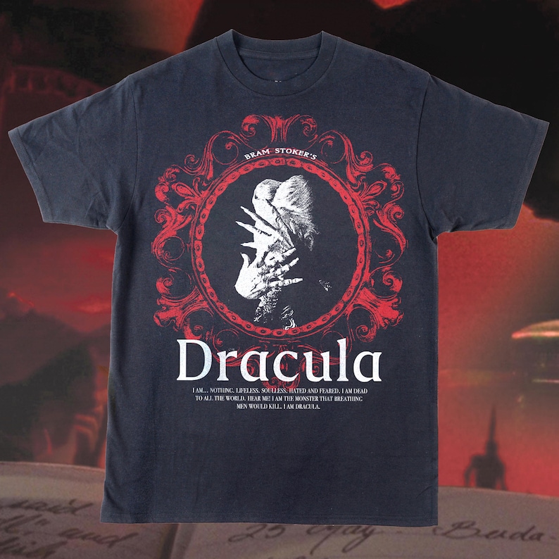 May include: Dark navy blue t-shirt featuring a red and white graphic of Dracula. The design includes the text "Bram Stoker's Dracula" and a quote from the novel. A classic horror-themed tee.