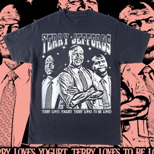 以下が含まれることがあります： 濃いネイビーブルーのTシャツ。スーツを着た3人の男性のグラフィックと「TERRY JEFFORDS」の文字がプリントされています。「TERRY LOVES YOGURT. TERRY LOVES TO BE LOVED」の文字がグラフィックの下にあります。背景はピンクと黒のデザインです。