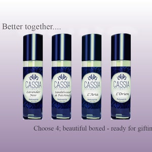 May include: Four 10 ml glass bottles of perfume oil with black caps and labels. The labels are white with blue and gold accents. The bottles are arranged in a row. The labels read "CASSIA AROMATICS" and the names of the scents: "Lavender Noir", "Sandalwood & Patchouli", "L'Aria", and "L'Orien". The text "Choose 4; beautiful boxed - ready for gifting" is below the bottles.