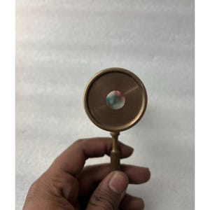 May include: A vintage brass kaleidoscope with a circular viewing lens. The kaleidoscope has a small handle and a colorful interior visible through the lens. The brass has a warm, aged patina.
