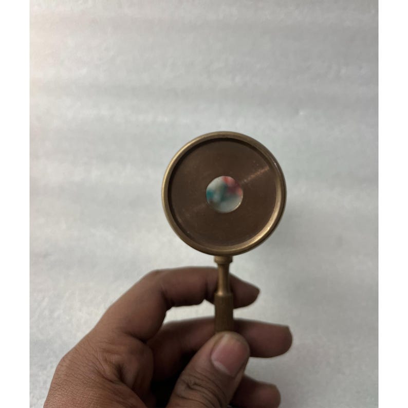 May include: A vintage brass kaleidoscope with a circular viewing lens. The kaleidoscope has a small handle and a colorful interior visible through the lens. The brass has a warm, aged patina.
