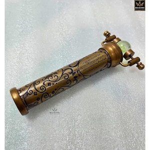 May include: A vintage brass kaleidoscope with an ornate floral design and the text "Life is like me ever a shifting kaleidoscope, a slight change, and all patterns alter." The kaleidoscope has a green glass lens.