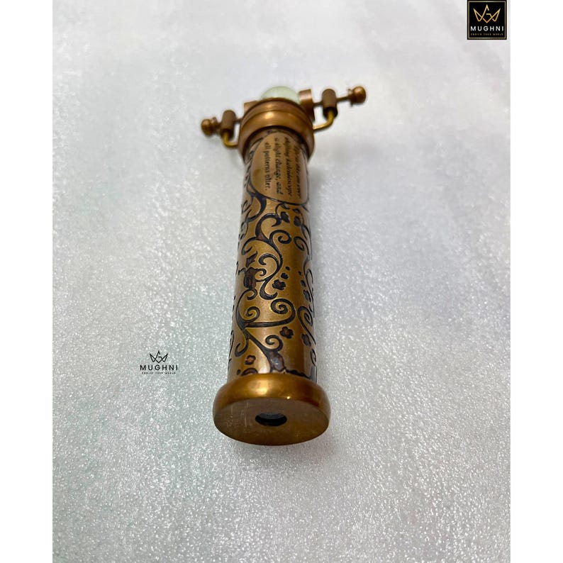 May include: A vintage-style brass kaleidoscope with intricate floral patterns etched on its body. The kaleidoscope features a rotating eyepiece and a small, glowing element at the top. The design includes a small amount of text.