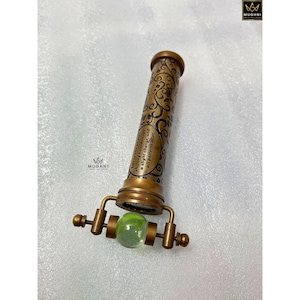 May include: A vintage brass kaleidoscope with ornate detailing and a green glass marble at the viewing end. The barrel features a quote: "Life is like a shifting kaleidoscope, a slight change, and all patterns alter."