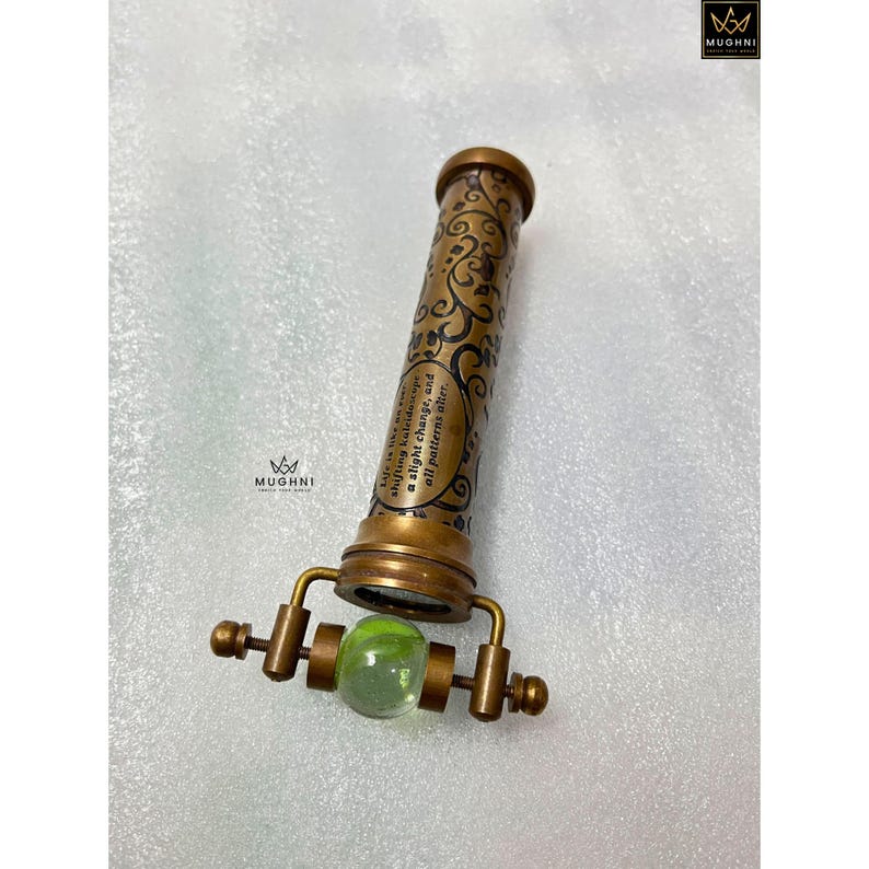 May include: A vintage brass kaleidoscope with ornate detailing and a green glass marble at the viewing end. The barrel features a quote: "Life is like a shifting kaleidoscope, a slight change, and all patterns alter."