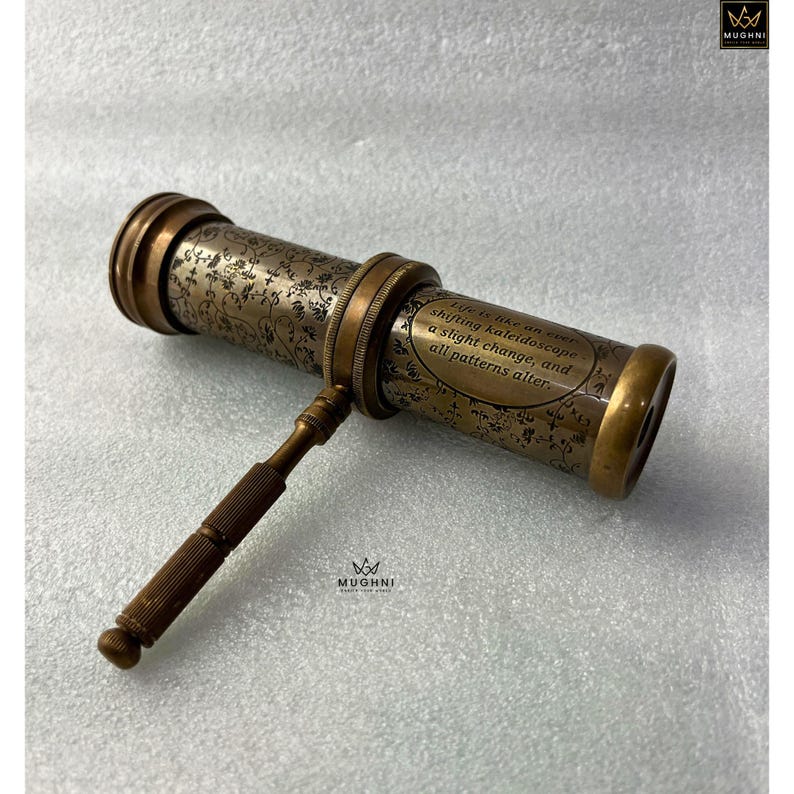May include: An antique brass kaleidoscope with floral engravings and a handle. The text on the side reads, "Life is like an ever-shifting kaleidoscope, a slight change, and all patterns alter."