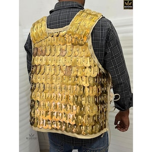 May include: A golden-colored, scale-mail vest with a cream-colored leather backing. The vest is made of overlapping metal plates, and is designed to be worn over the torso. The vest is a historical garment, likely for costume or display.