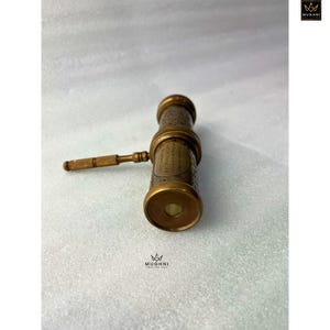 May include: A vintage brass telescope with a wooden handle. The telescope has intricate engraved details and a classic design. The brass has a warm, aged patina. The handle is a light brown color. The telescope is a nautical or antique-themed item.