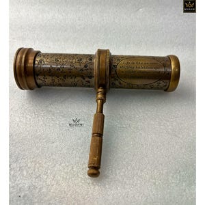 May include: A vintage brass kaleidoscope with floral engravings and the text "Life is like an ever-shifting kaleidoscope..." The antique toy has a handle and decorative end caps. The brass has a warm, aged patina.