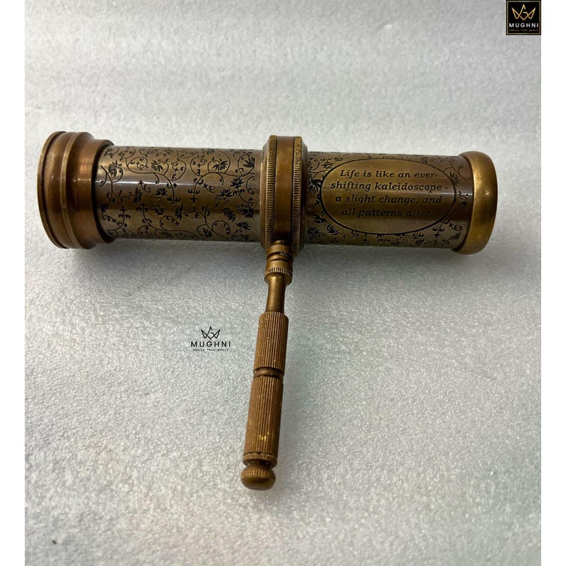 May include: A vintage brass kaleidoscope with floral engravings and the text "Life is like an ever-shifting kaleidoscope..." The antique toy has a handle and decorative end caps. The brass has a warm, aged patina.