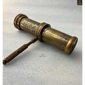 May include: Antique brass kaleidoscope with floral engravings and the quote "Life is like an ever-shifting kaleidoscope - a slight change, and all patterns alter." The vintage toy has a handle and is on a white surface.