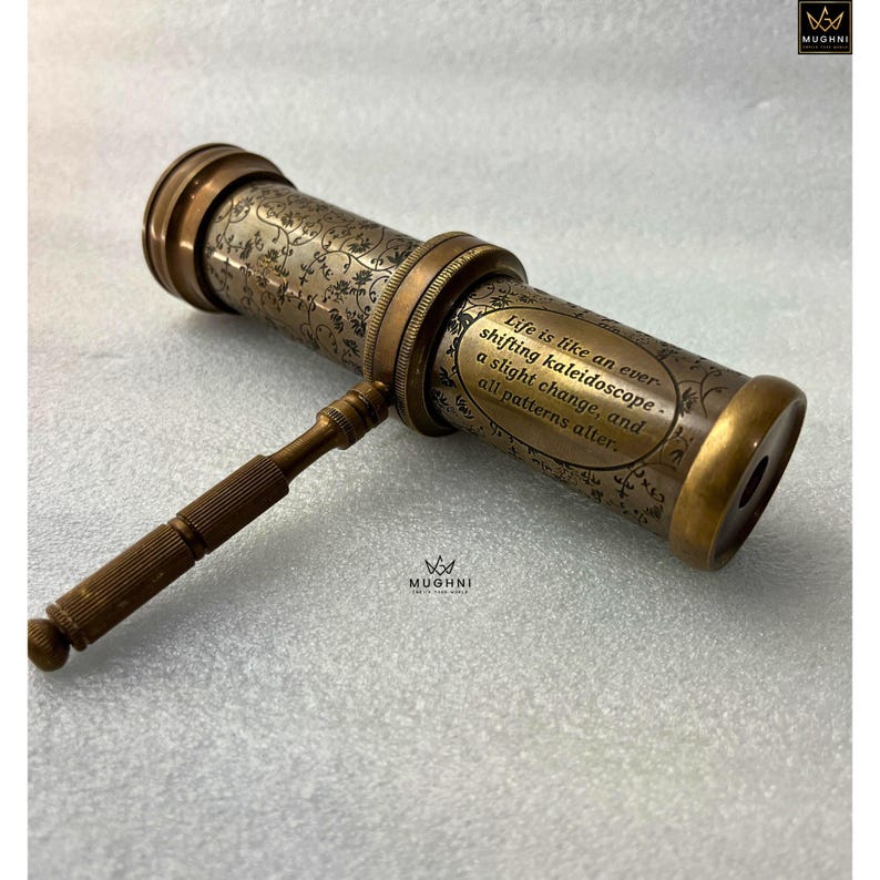 May include: Antique brass kaleidoscope with floral engravings and the quote "Life is like an ever-shifting kaleidoscope - a slight change, and all patterns alter." The vintage toy has a handle and is on a white surface.