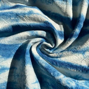 Może przedstawiać: Zbliżenie na tkaninę w kolorze niebieskim i białym z efektem tie-dye. Tkanina jest złożona i skręcona, tworząc wirujący wzór.