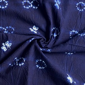 Può includere: Tessuto blu scuro con motivi floreali e circolari bianchi. Il tessuto è stropicciato, creando ombre e consistenza. Il design presenta piccoli fiori bianchi stilizzati e motivi circolari.