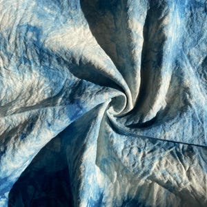 Może przedstawiać: Zbliżenie na tkaninę w kolorze niebieskim i białym, farbowaną metodą tie-dye. Tkanina jest pomięta i złożona, tworząc wirujący wzór.