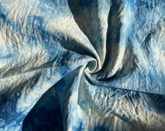 May include: A close-up of a blue and white tie-dyed fabric. The fabric is crumpled and folded, creating a swirling pattern.