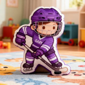 May include: A plush hockey player pillow in purple and white. The pillow features a cartoon hockey player wearing a helmet, jersey with the name "GARY", and hockey gear. The player is holding a hockey stick and puck.