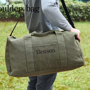 May include: A green canvas duffel bag with a black shoulder strap. The bag has a pocket on the front with the name "Benson" embroidered in black.