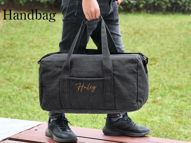 May include: A black canvas duffel bag with a zipper closure and a top handle. The bag has a pocket on the front with the name "Haley" embroidered in orange thread.