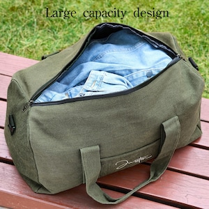 May include: A green canvas duffel bag with a zipper closure and a black strap. The bag is open and filled with blue denim clothing. The text "Large capacity design" is visible at the top of the image.