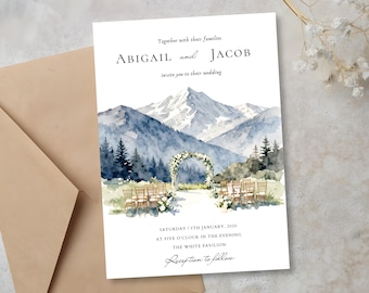Puede incluir: Invitación de boda con una escena de montaña en acuarela en tonos azules y grises. La invitación incluye los nombres "ABIGAIL y JACOB" y los detalles del evento. Un sobre marrón es parcialmente visible a la izquierda.