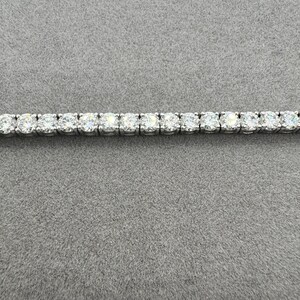 May include: A tennis bracelet with a continuous row of round-cut diamonds set in a silver-coloured metal. The bracelet is shown against a grey background, highlighting the sparkle of the gemstones.