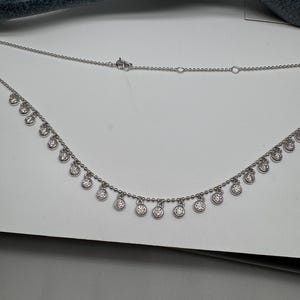 May include: A silver necklace with a delicate chain and small round pendants with clear stones.