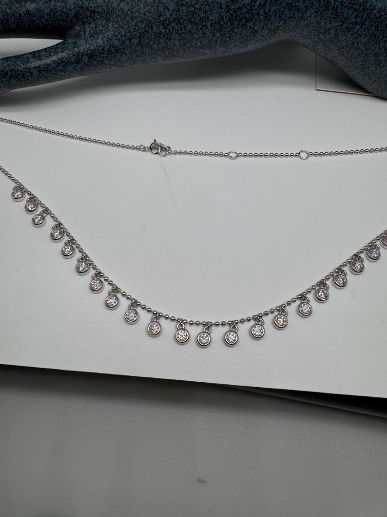 May include: A silver necklace with a delicate chain and small round pendants with clear stones.