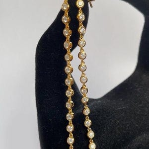 May include: A pair of long gold earrings with a chain of small round clear stones.