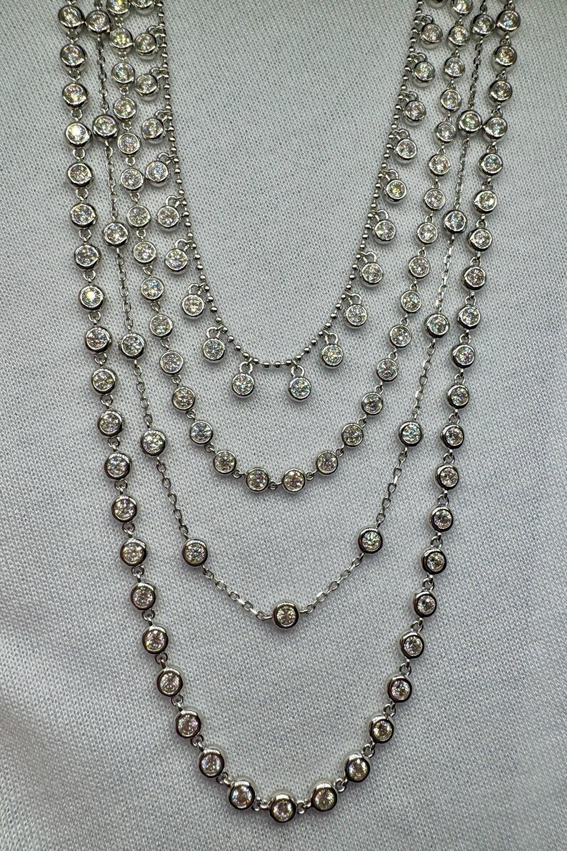 May include: A silver multi-strand necklace with round, clear stones. The necklace has a graduated length with the longest strand featuring a dangling design.