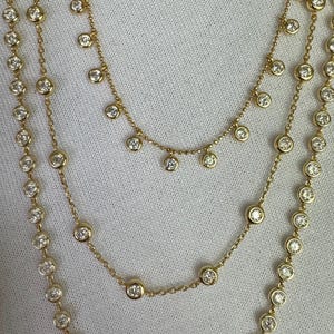 May include: A gold chain necklace with three strands of small round diamonds. The top strand has a dangling row of diamonds.