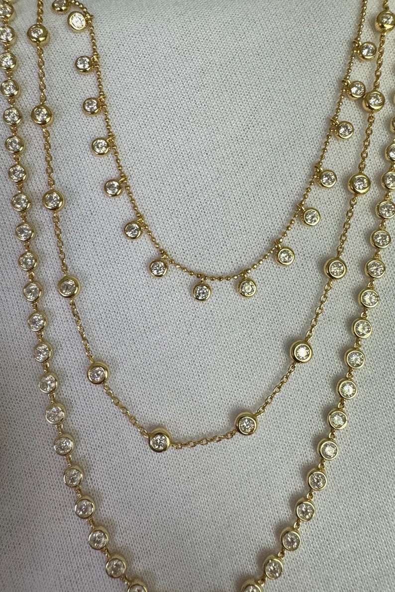 May include: A gold chain necklace with three strands of small round diamonds. The top strand has a dangling row of diamonds.
