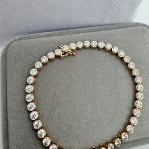 K&ouml;nnte beinhalten: Ein goldenes Tennisarmband mit runden, klaren Steinen.