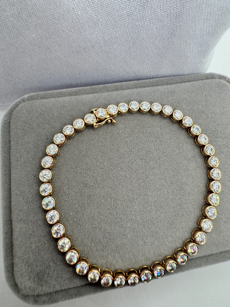 K&ouml;nnte beinhalten: Ein goldenes Tennisarmband mit runden, klaren Steinen.