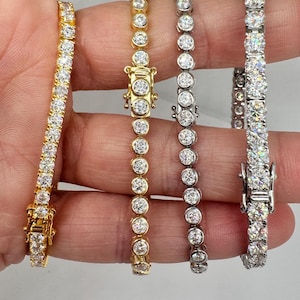 May include: Three tennis bracelets with round stones. The bracelets are in gold, silver, and white gold.