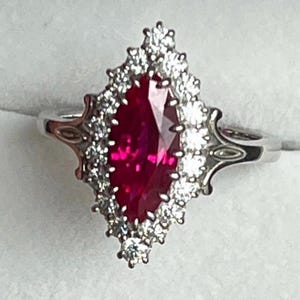 May include: A silver ring with a large, red, marquise-shaped ruby surrounded by a halo of smaller, white diamonds.