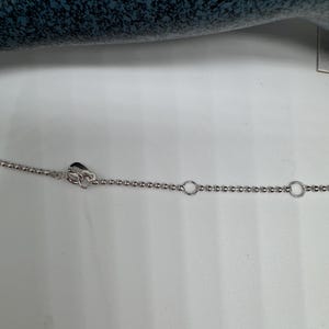 May include: A silver chain necklace with a heart-shaped clasp and two circular links.