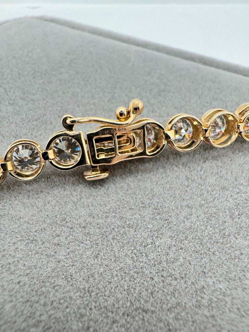 K&ouml;nnte beinhalten: Ein goldenes Kettenarmband mit einem Verschluss, auf dem "14K 0.9 ACW" steht. Das Armband besteht aus runden Steinen.