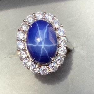 May include: A silver ring with a large blue star sapphire surrounded by a halo of smaller clear stones.