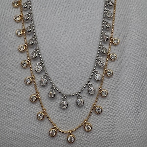 May include: A layered necklace with a gold chain and two silver chains. Each chain has small round clear stones hanging from it.